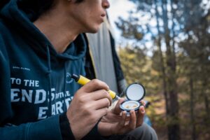 A young man pokes out of a camping tent to take a dab of cannabis concentrate using a Dip Devices Dipper dab straw.